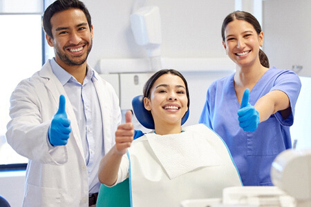dentist, dental assistant, and patient giving thumbs up