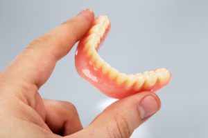 Hand holding lower denture between thumb and forefinger