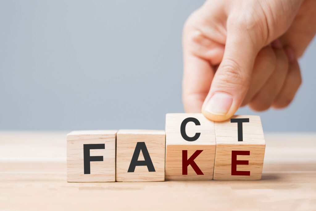 Hands flipping wood blocks from "FACT" to "FAKE"